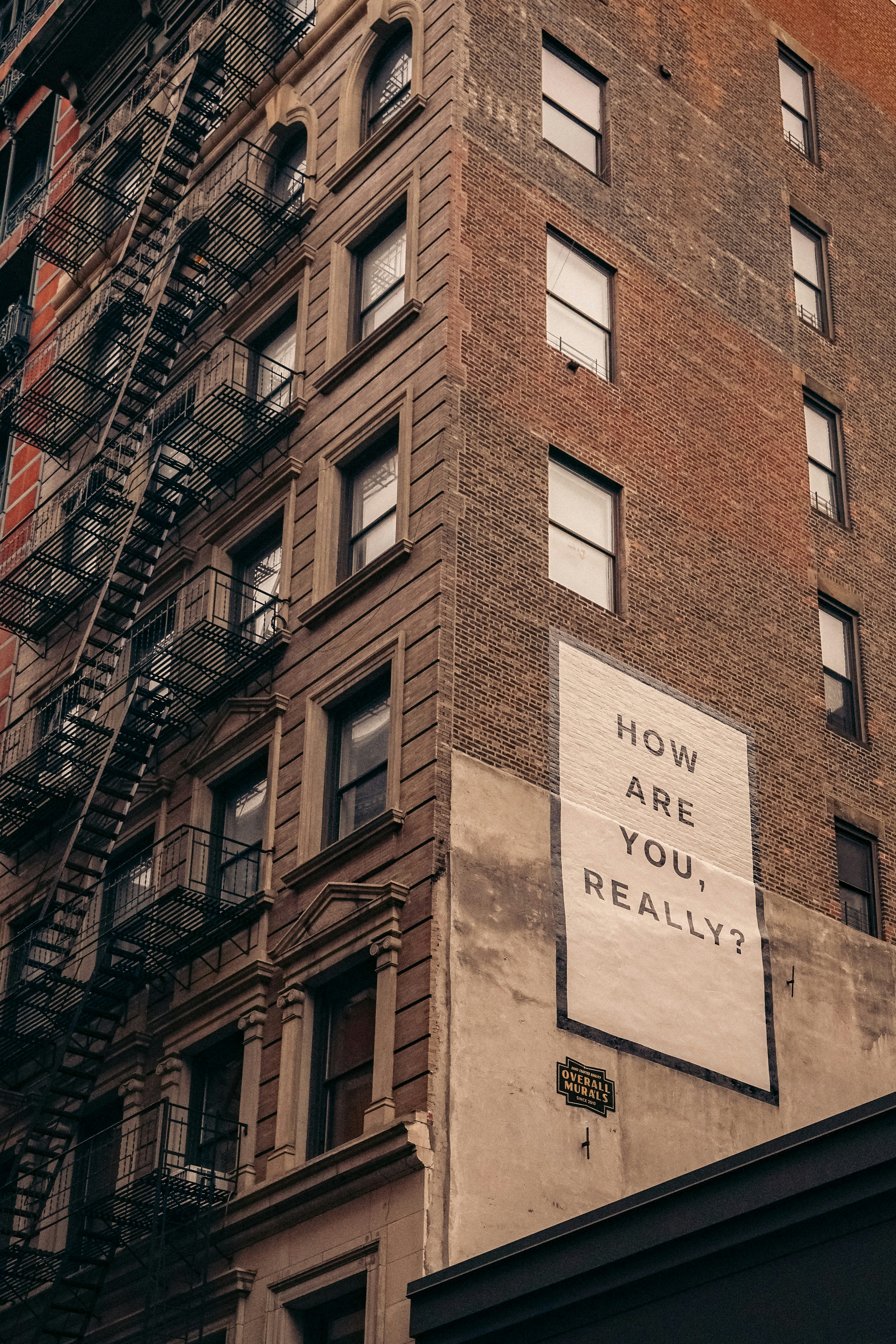 Mural reading 'How are you, really?' on a New York City brick building